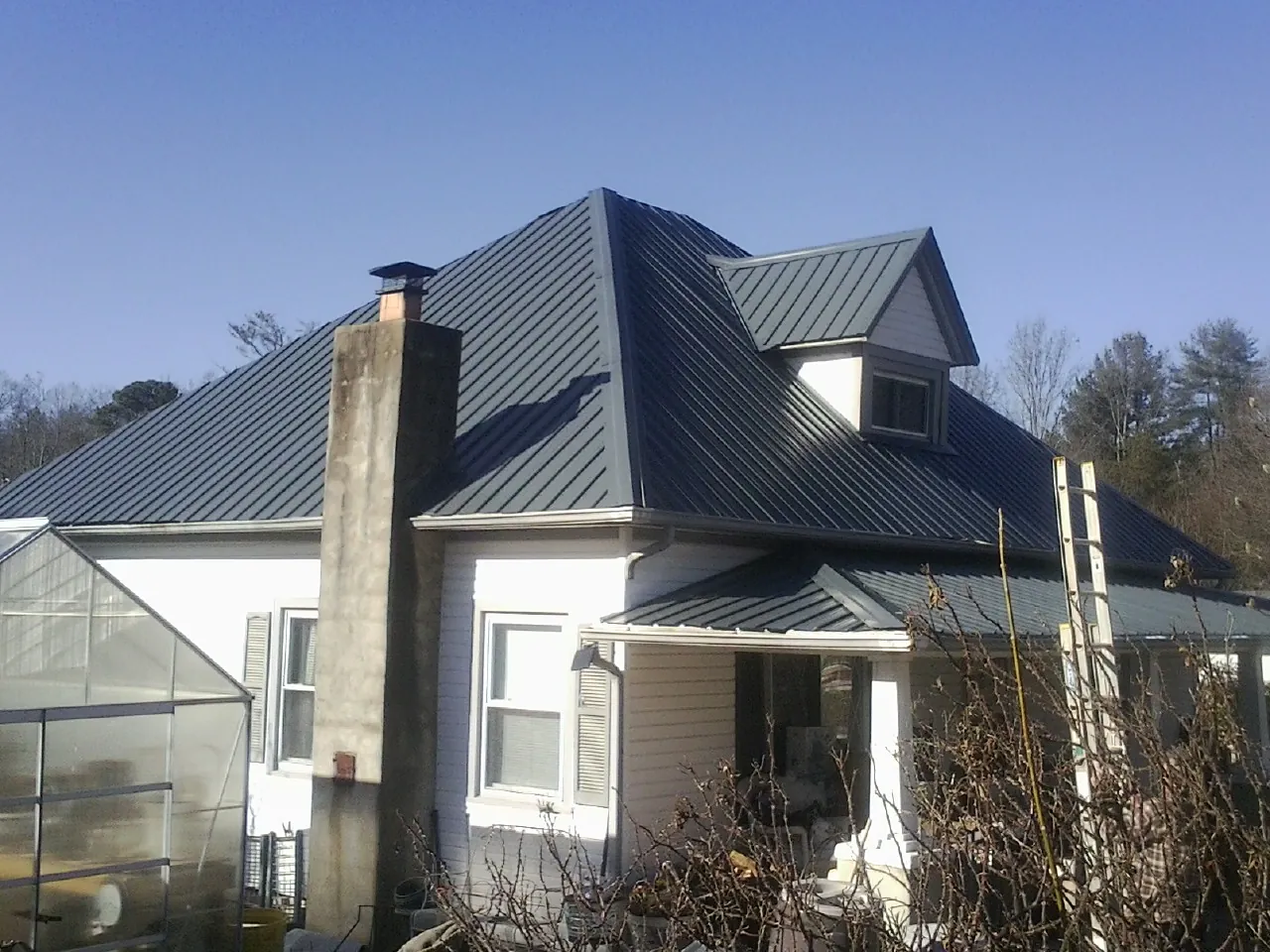 Dark blue standing seam metal roof on a white farmhouse with dormer — Slate & Tile Roof Repair by Roofing Brothers in Schoenchen