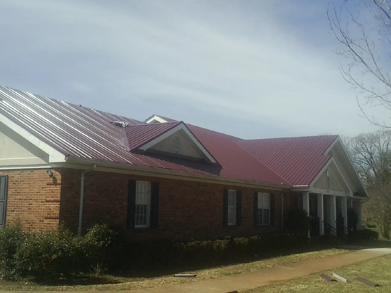 Red metal roof with gabled entries on a long brick building, from a Hail Damage Roof Repair job in Schoenchen