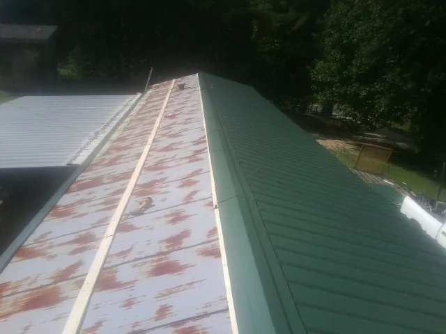 Old rusted panels beside newly installed green metal roofing — Wind Damage Roof Repair by Roofing Brothers in Schoenchen