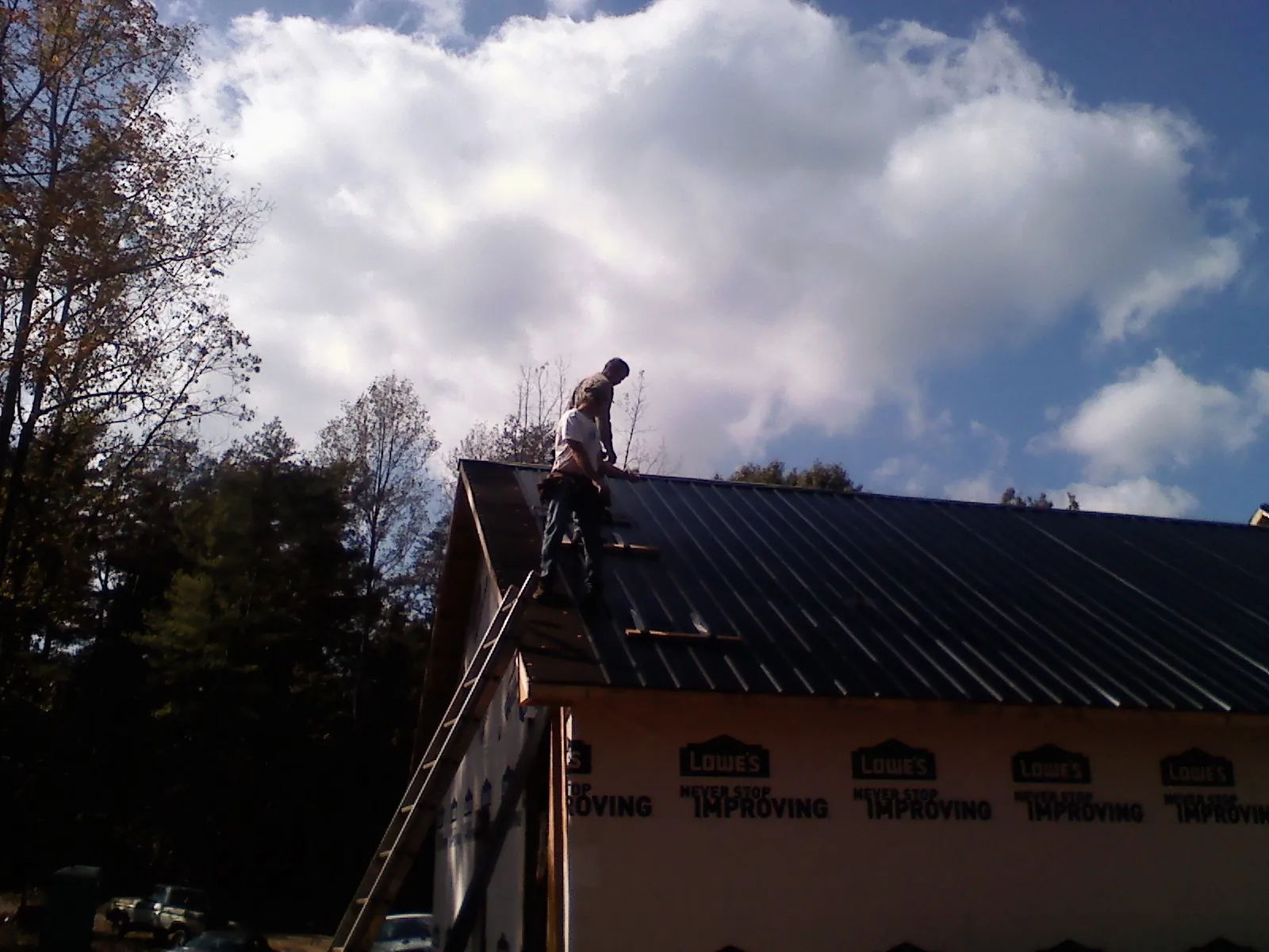 Roofer fastening dark metal panels high against a cloudy sky, from a Roof Inspection job in Schoenchen