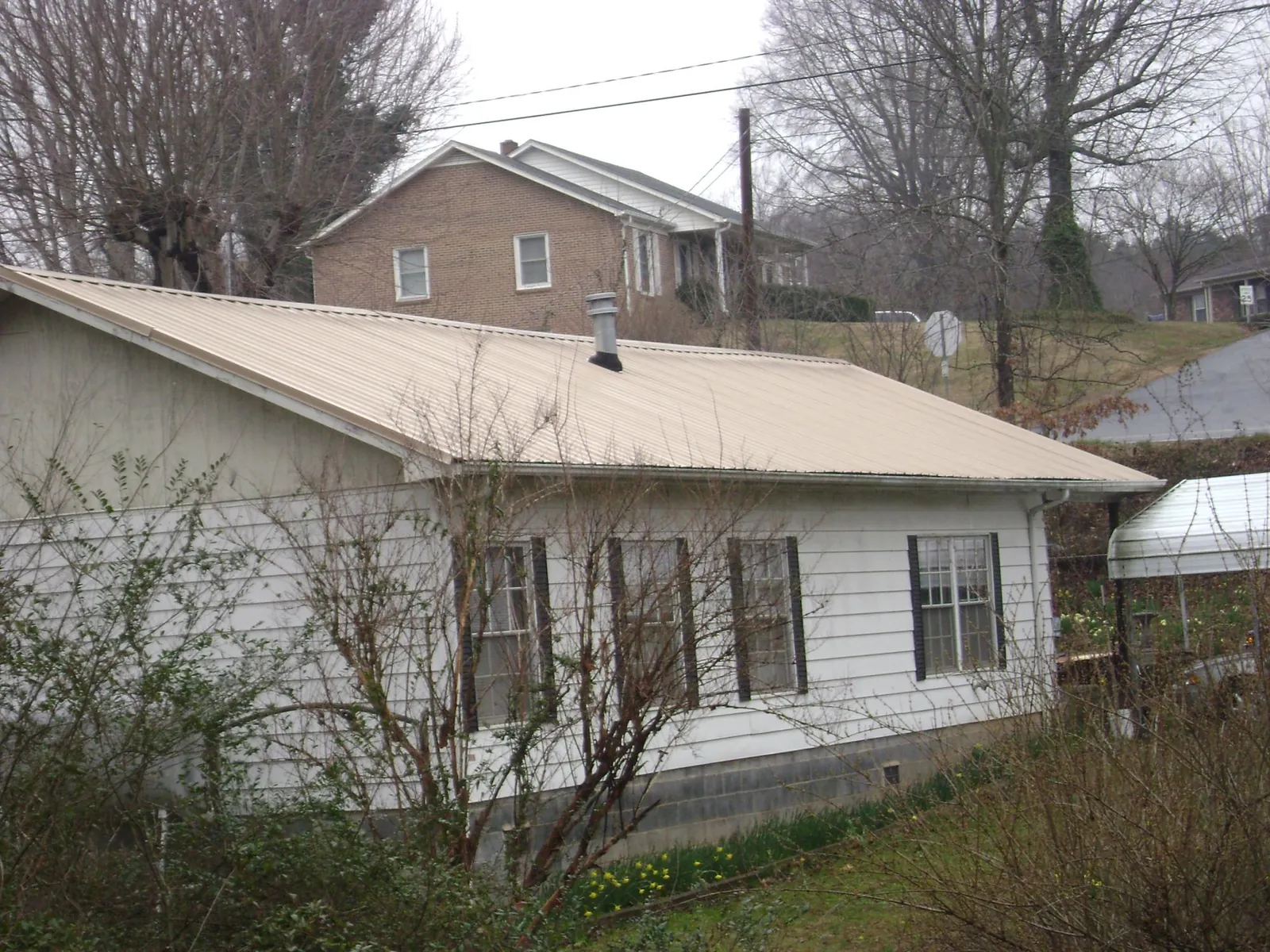Tan metal roof on a white sided house set into a hillside — Commercial Roofing by Roofing Brothers in Schoenchen